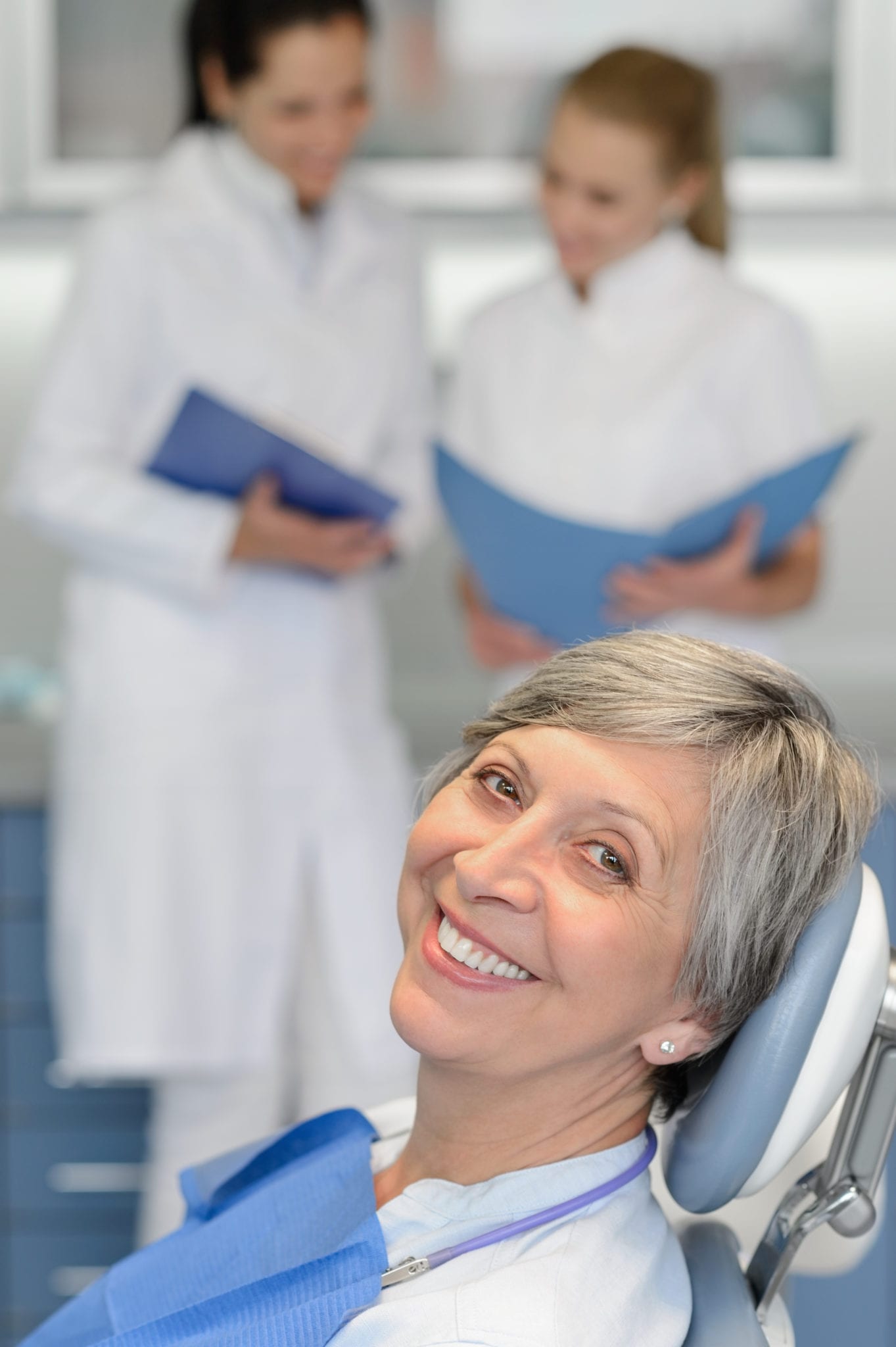 Mature Female In Dental Chair With Doctors in the Background