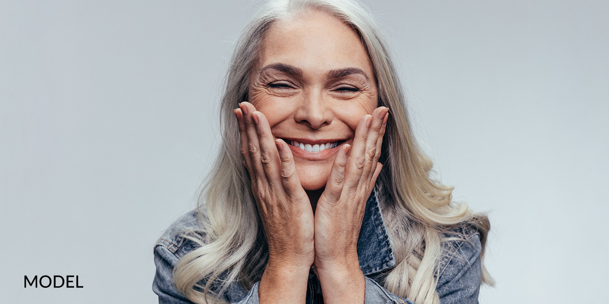 Older Female Holding Cheeks With Hands Smiling After Oral Surgery