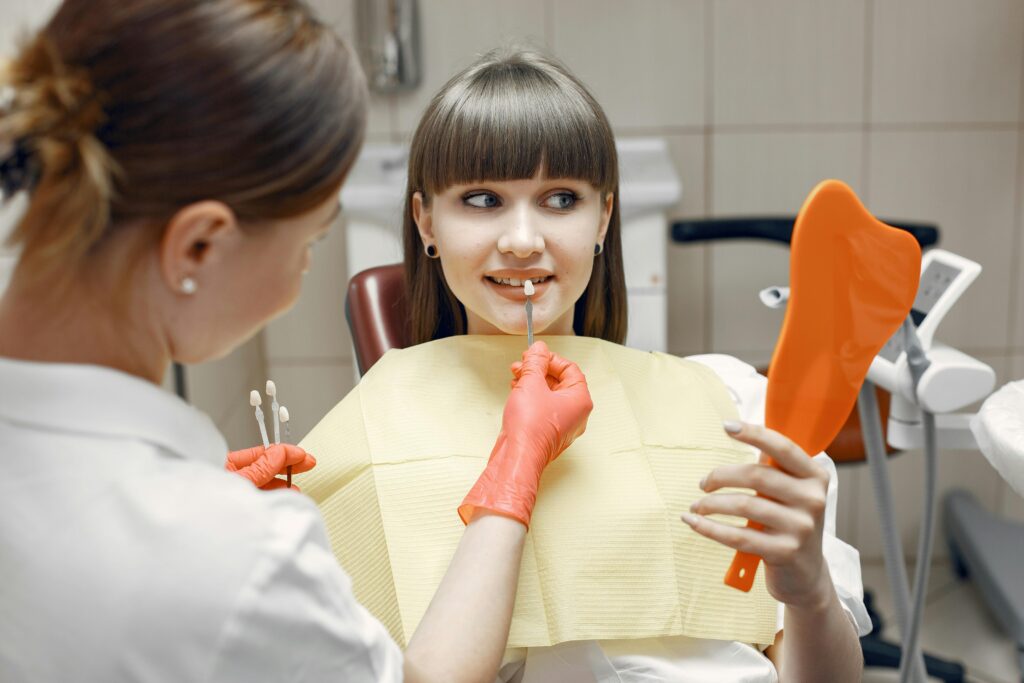 Dentist consults a young woman on veneers using dental tools and mirror in a clinic.